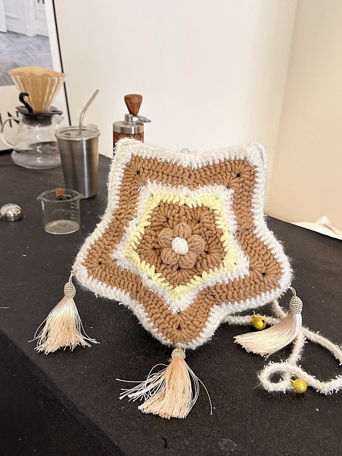 Handwoven star-shaped knit bag with soft knit material, tassel accents, and a mix of brown, white, and yellow colors, perfect for daily use or decoration.