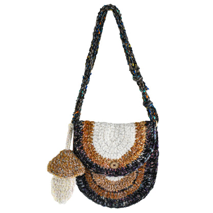 Handmade crochet crossbody bag with earthy tones, featuring a unique mushroom charm, semi-circle flap design, and durable woven strap. Lightweight and eco-friendly, perfect for boho and vintage-inspired styles.