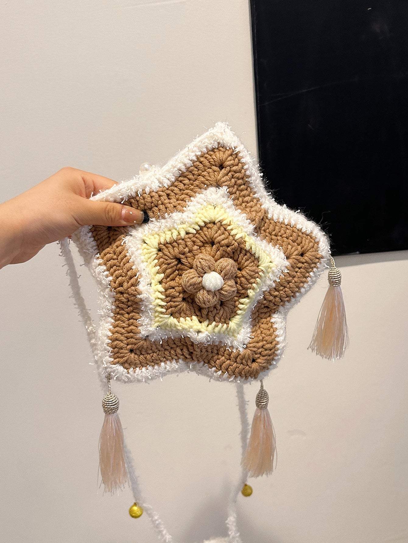 Handwoven star-shaped knit bag with soft knit material, tassel accents, and a mix of brown, white, and yellow colors, perfect for daily use or decoration.