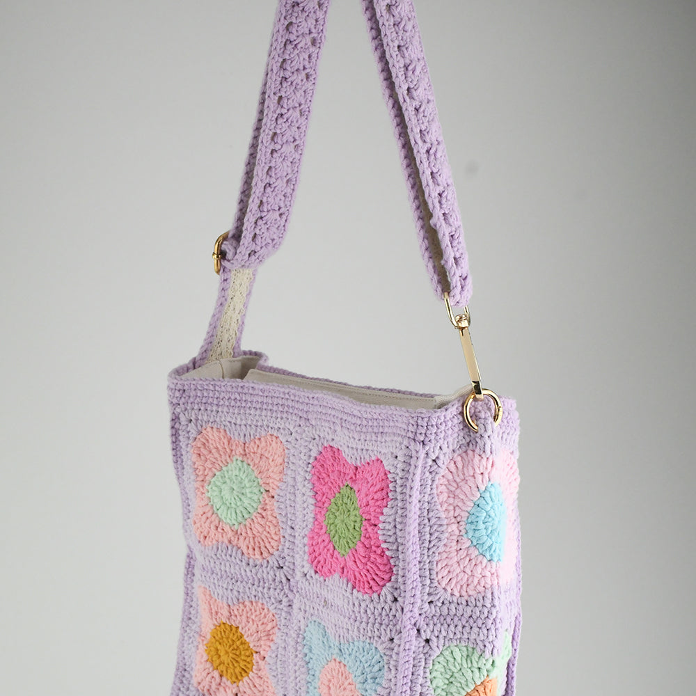 A handmade crochet shoulder bag with a lavender base and colorful floral square patterns. The bag features an adjustable and detachable strap, a soft texture, and a spacious interior, perfect for daily use or casual outings.