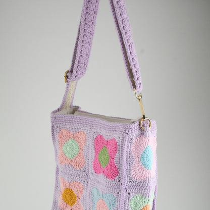 A handmade crochet shoulder bag with a lavender base and colorful floral square patterns. The bag features an adjustable and detachable strap, a soft texture, and a spacious interior, perfect for daily use or casual outings.