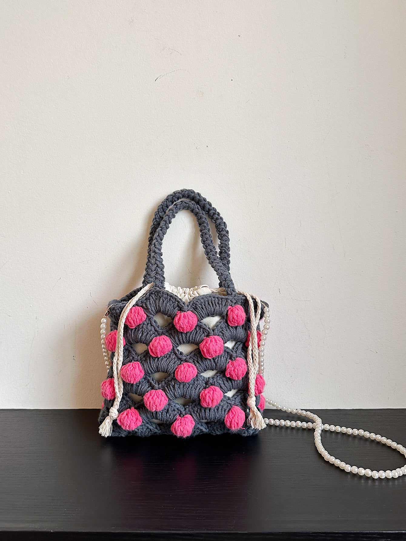 Handwoven tote bag with a gray woven base and pink circular accents, adorned with pearl chain details. Unique design, perfect for daily use or shopping.