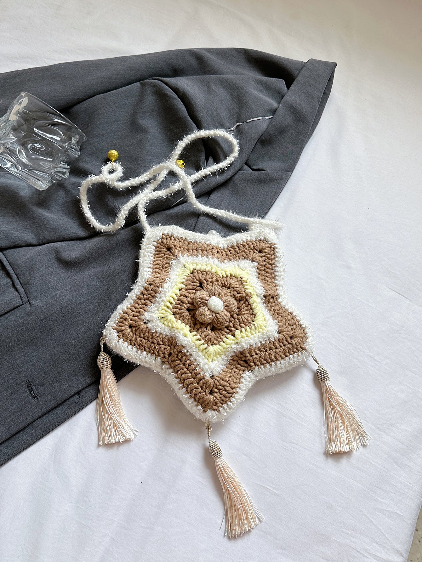 Handwoven star-shaped knit bag with soft knit material, tassel accents, and a mix of brown, white, and yellow colors, perfect for daily use or decoration.