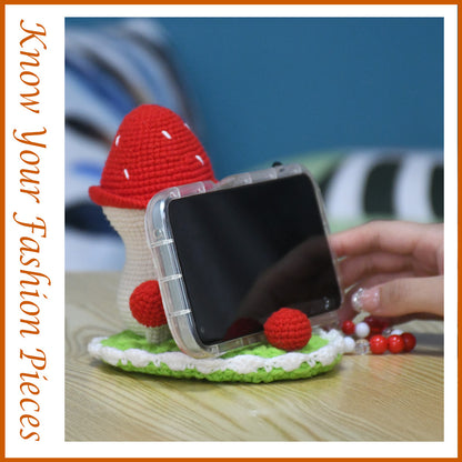 Decorative crochet toadstool cottage featuring bright red cap with white dots, beige body, and green circular base
