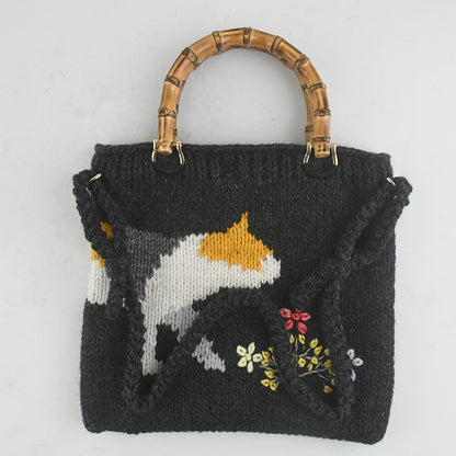 Handmade knitted black tote bag featuring a bamboo handle, embroidered cat design, and colorful floral accents. Lightweight and eco-friendly, perfect for casual or creative fashion styles.