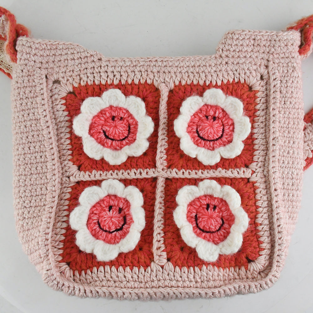 Handmade pink crochet bag with red and white floral square patterns, featuring a top handle. Perfect for casual outings or shopping