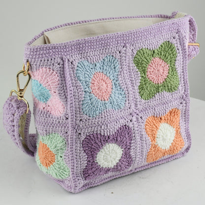 A handmade crochet shoulder bag with a lavender base and colorful floral square patterns. The bag features an adjustable and detachable strap, a soft texture, and a spacious interior, perfect for daily use or casual outings.