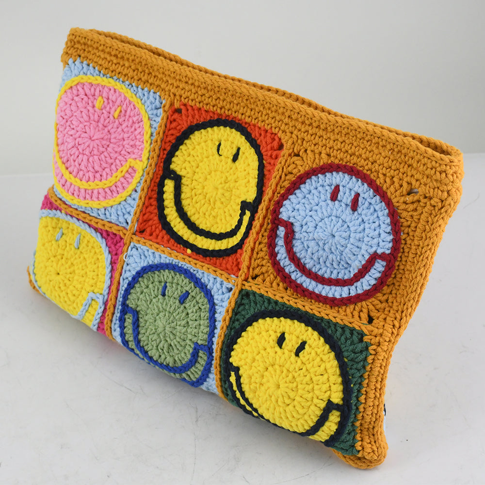 Handmade crochet clutch bag featuring colorful smiling face motifs in pink, yellow, blue, green, red, and orange squares. Lightweight, eco-friendly, and compact design with a secure zipper closure.