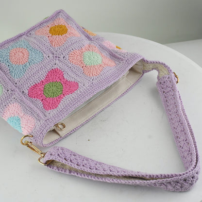 A handmade crochet shoulder bag with a lavender base and colorful floral square patterns. The bag features an adjustable and detachable strap, a soft texture, and a spacious interior, perfect for daily use or casual outings.