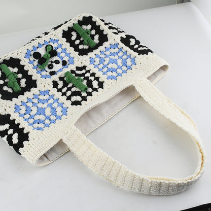 Handmade crochet tote bag featuring a panda design with bamboo patterns, blue and black square details, and a soft white base. Perfect for casual outings or eco-friendly shopping.