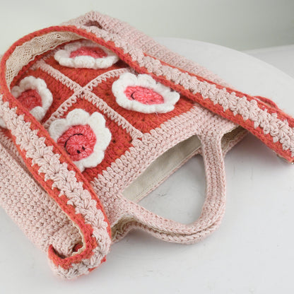 Handmade pink crochet bag with red and white floral square patterns, featuring a top handle. Perfect for casual outings or shopping