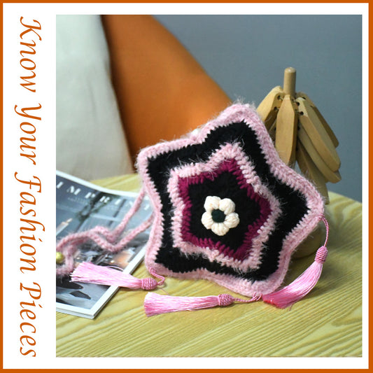 Handmade star-shaped crochet bag in pink and black with three pink tassels, white flower center, and braided shoulder strap
